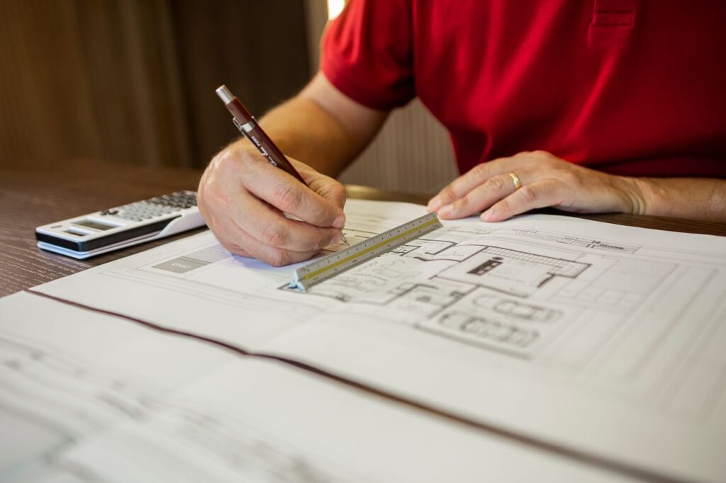 Architect working on floor plans with ruler and pencil in an office setting.