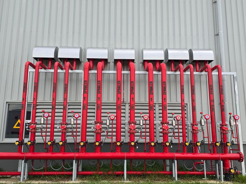 Red industrial fire sprinkler pipes aligned on a factory exterior wall.